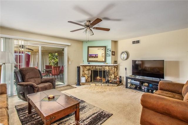 carpeted living room featuring ceiling fan and a stone fireplace