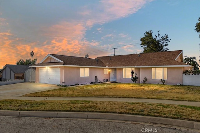 ranch-style home featuring driveway, a garage, a lawn, fence, and stucco siding