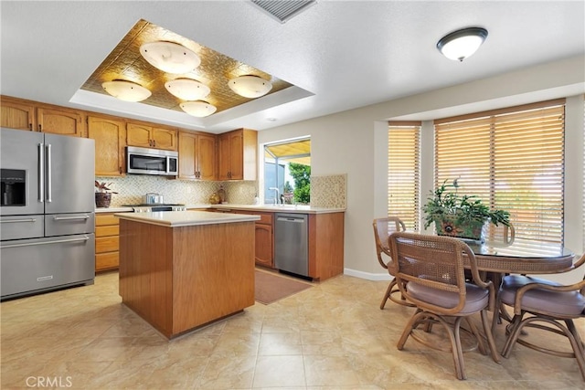 kitchen featuring a raised ceiling, tasteful backsplash, stainless steel appliances, and a center island