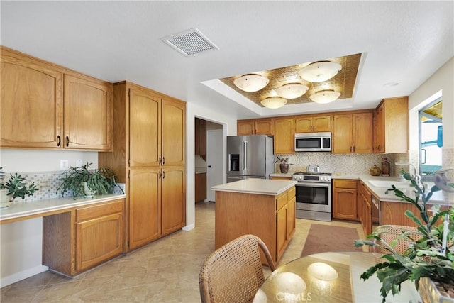 kitchen featuring stainless steel appliances, tasteful backsplash, a tray ceiling, a center island, and sink