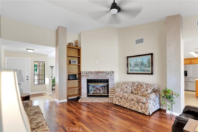 living room featuring vaulted ceiling, ceiling fan, hardwood / wood-style floors, and a brick fireplace