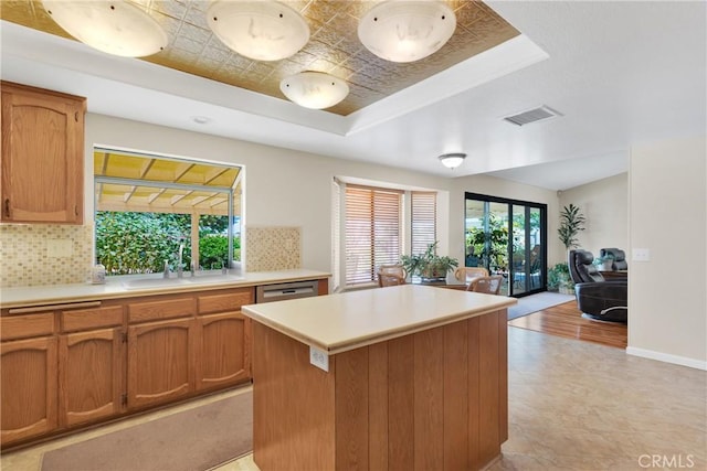 kitchen featuring backsplash, a raised ceiling, sink, stainless steel dishwasher, and a center island