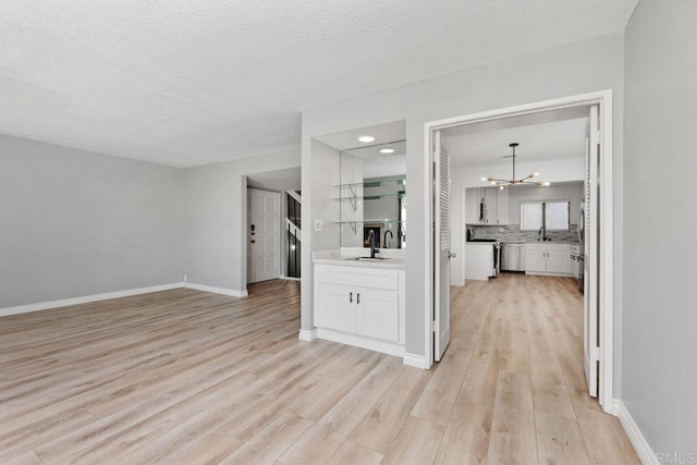 unfurnished living room featuring a textured ceiling, sink, light hardwood / wood-style floors, and a notable chandelier