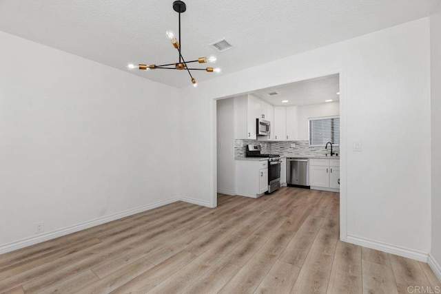 kitchen featuring appliances with stainless steel finishes, tasteful backsplash, hanging light fixtures, white cabinets, and sink