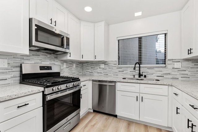 kitchen featuring light stone countertops, stainless steel appliances, white cabinetry, and sink