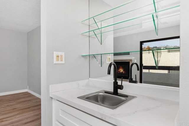 kitchen with light stone counters, sink, white cabinetry, and hardwood / wood-style flooring