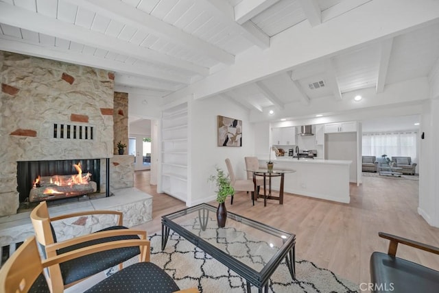 living room featuring plenty of natural light, beam ceiling, a fireplace, and light hardwood / wood-style flooring