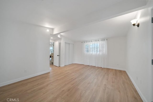 spare room featuring light wood-type flooring and vaulted ceiling with beams