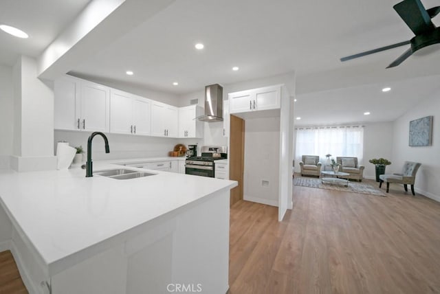 kitchen featuring kitchen peninsula, stainless steel gas stove, wall chimney exhaust hood, white cabinets, and sink