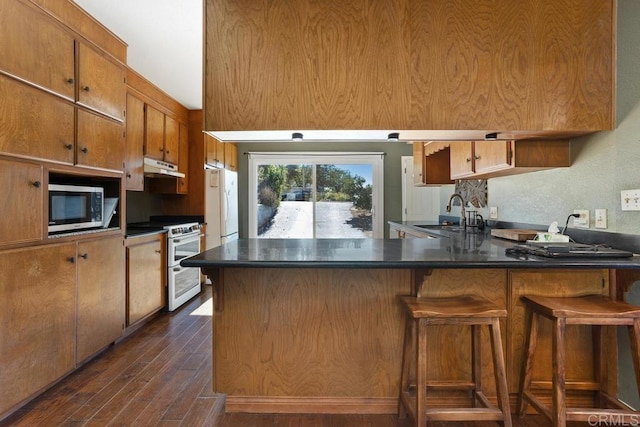 kitchen with kitchen peninsula, white appliances, a kitchen breakfast bar, dark wood-type flooring, and sink