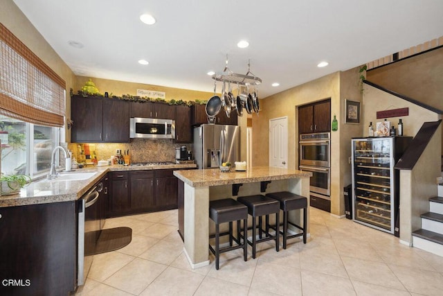 kitchen featuring a center island, sink, dark brown cabinetry, appliances with stainless steel finishes, and beverage cooler