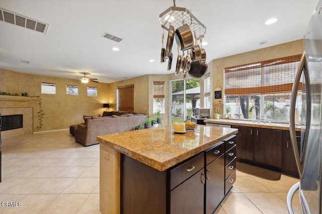 kitchen with a kitchen island, stainless steel refrigerator, light tile patterned flooring, ceiling fan, and dark brown cabinets