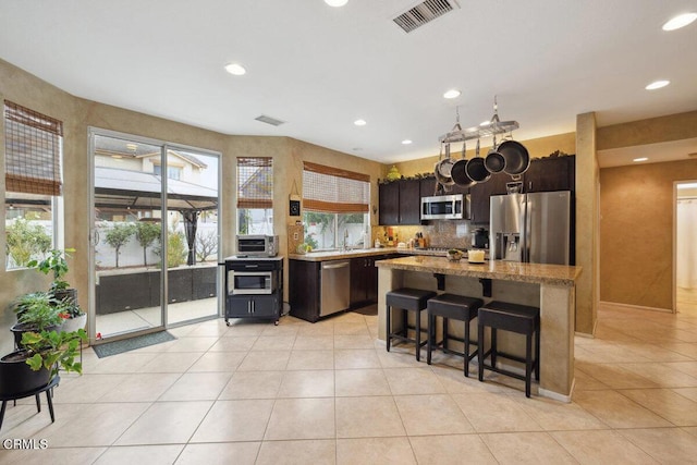 kitchen with light tile patterned floors, stainless steel appliances, a kitchen bar, and a center island