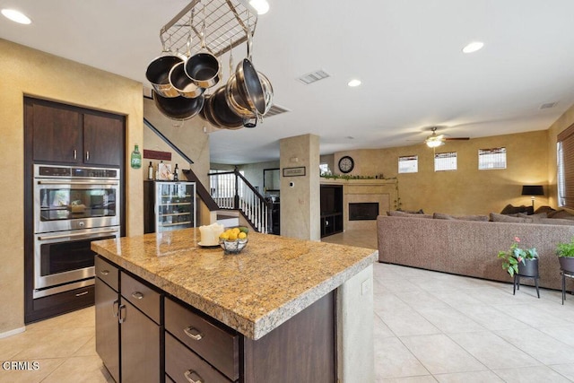 kitchen featuring ceiling fan, a kitchen island, stainless steel double oven, dark brown cabinets, and beverage cooler