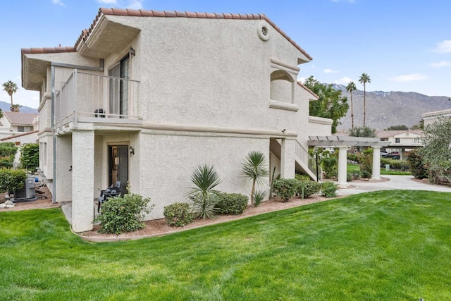 back of house featuring a mountain view, a balcony, a yard, central AC unit, and a pergola