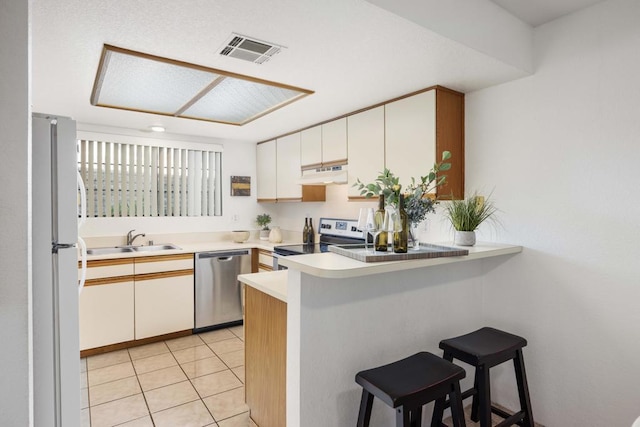 kitchen with kitchen peninsula, light tile patterned flooring, a kitchen breakfast bar, stainless steel appliances, and white cabinets