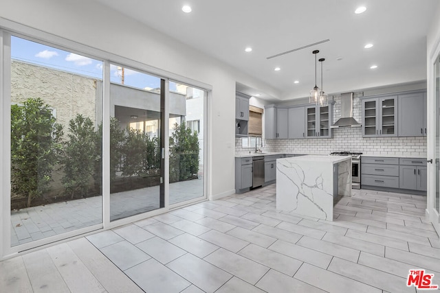 kitchen with stainless steel appliances, gray cabinetry, wall chimney range hood, a kitchen island, and pendant lighting