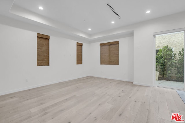 empty room with light hardwood / wood-style floors and a tray ceiling