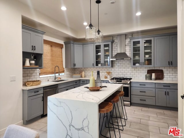 kitchen featuring appliances with stainless steel finishes, a center island, decorative light fixtures, wall chimney range hood, and sink