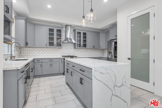 kitchen with gray cabinets, appliances with stainless steel finishes, a tray ceiling, wall chimney range hood, and a kitchen island