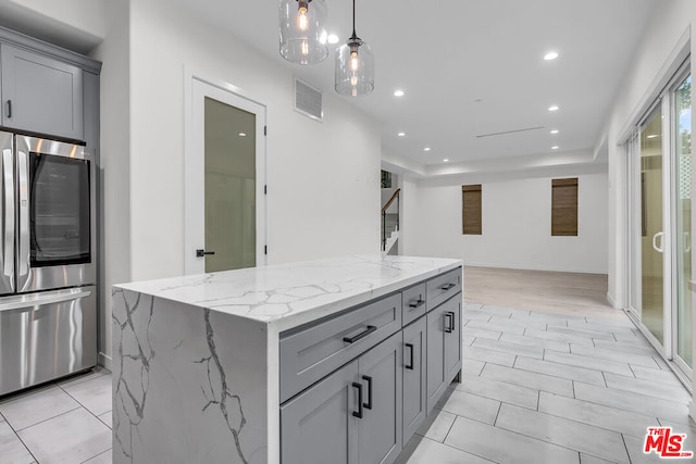 kitchen featuring gray cabinets, stainless steel fridge, light stone counters, and a center island