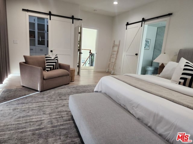 bedroom featuring connected bathroom, hardwood / wood-style floors, and a barn door