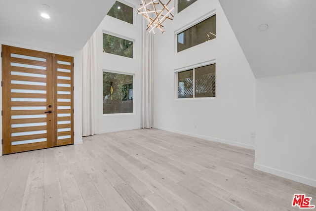 entryway with light hardwood / wood-style floors, a high ceiling, and an inviting chandelier