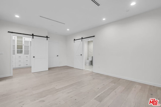 unfurnished bedroom featuring ensuite bathroom, a barn door, and light wood-type flooring