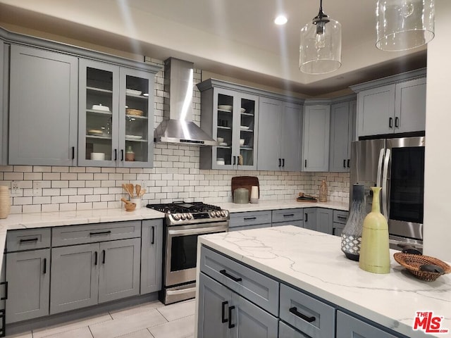 kitchen with tasteful backsplash, wall chimney range hood, gray cabinets, pendant lighting, and appliances with stainless steel finishes