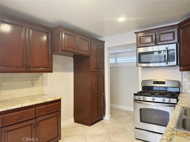 kitchen with backsplash, sink, light stone countertops, stainless steel appliances, and light tile patterned floors