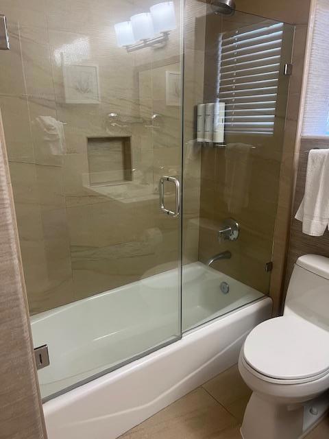 bathroom featuring toilet, tile patterned flooring, and enclosed tub / shower combo