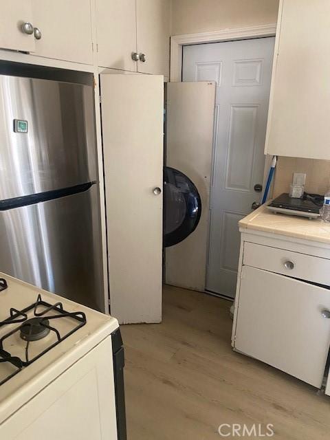 kitchen featuring stainless steel fridge, white range with gas cooktop, white cabinets, and light hardwood / wood-style flooring