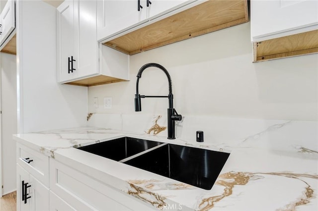 kitchen with white cabinetry, sink, and light stone counters