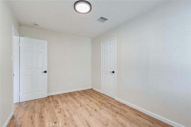 empty room featuring light wood-style floors, visible vents, and baseboards