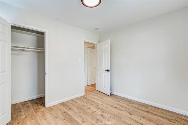 unfurnished bedroom featuring a closet, light wood-type flooring, and baseboards