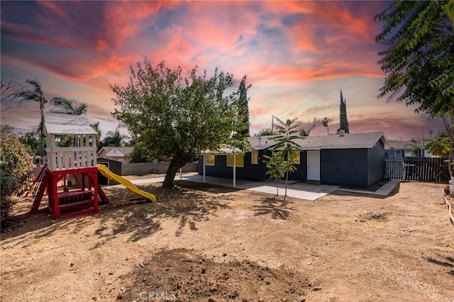 yard at dusk with a patio area, a playground, and fence