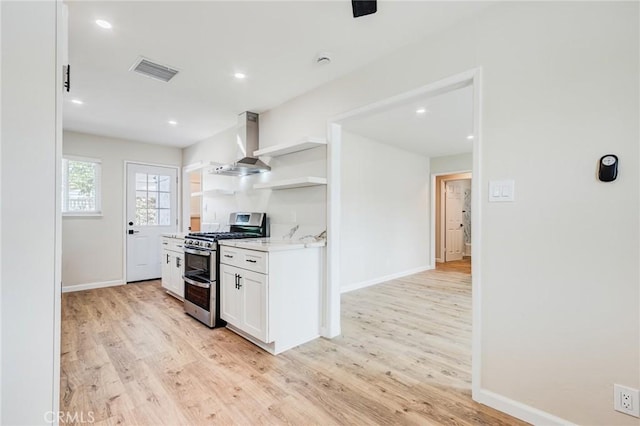 kitchen featuring wall chimney range hood, light hardwood / wood-style flooring, light stone counters, white cabinets, and range with two ovens