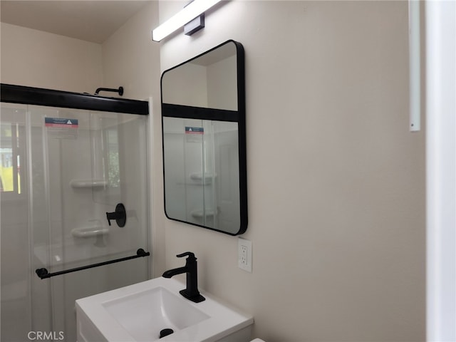 bathroom featuring a shower with shower door and a sink