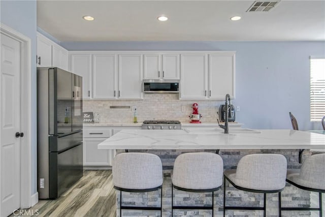 kitchen with light stone counters, a kitchen breakfast bar, white cabinetry, and appliances with stainless steel finishes