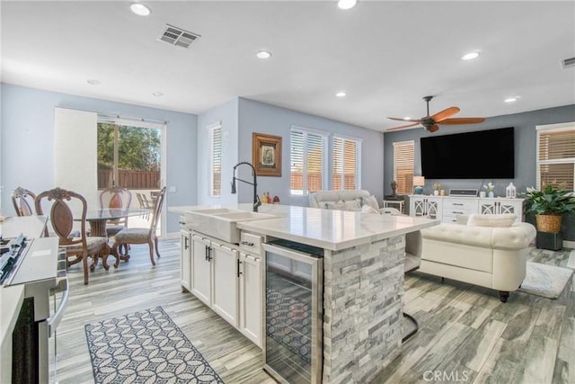 kitchen featuring wine cooler, ceiling fan, a center island with sink, sink, and white cabinetry