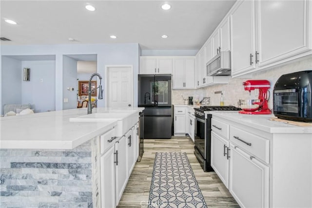 kitchen with stainless steel appliances, backsplash, white cabinetry, and an island with sink