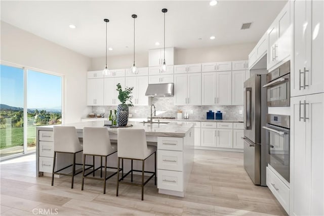 kitchen featuring tasteful backsplash, a center island with sink, a kitchen bar, hanging light fixtures, and white cabinets