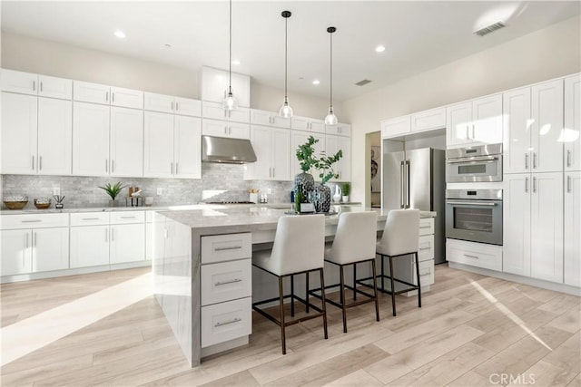 kitchen with a kitchen breakfast bar, white cabinetry, backsplash, and an island with sink