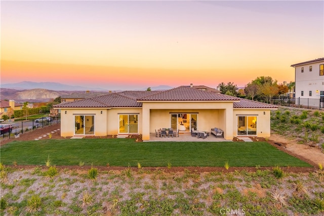 back house at dusk with a lawn, a mountain view, and a patio