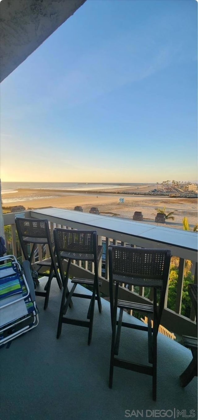 balcony at dusk featuring a water view and a view of the beach