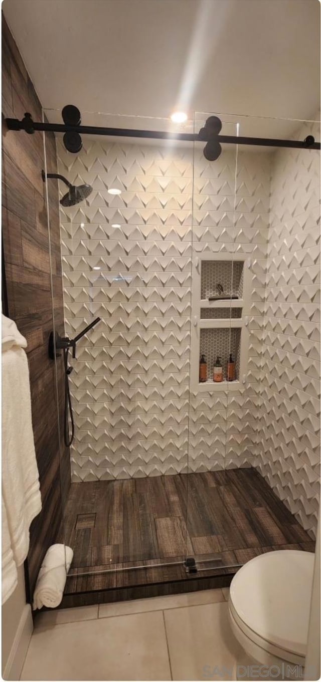 bathroom with toilet, tile patterned flooring, and a tile shower