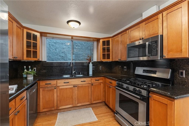 kitchen featuring stainless steel appliances, dark stone counters, light hardwood / wood-style floors, sink, and backsplash