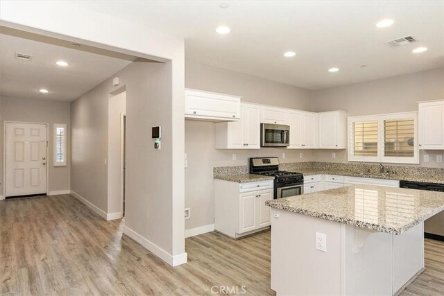 kitchen with white cabinets, light stone counters, stainless steel appliances, and a kitchen island