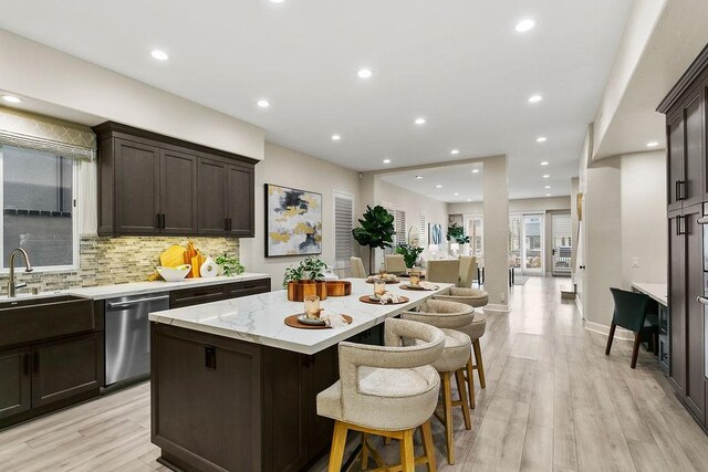 kitchen with a kitchen island, a kitchen breakfast bar, sink, stainless steel dishwasher, and light hardwood / wood-style flooring