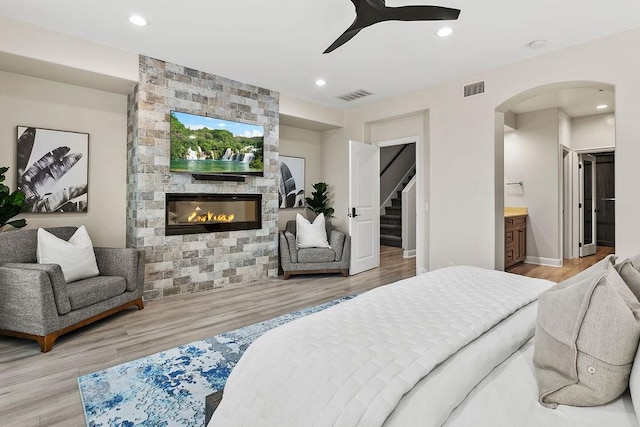 bedroom with ceiling fan, a fireplace, connected bathroom, and light hardwood / wood-style floors